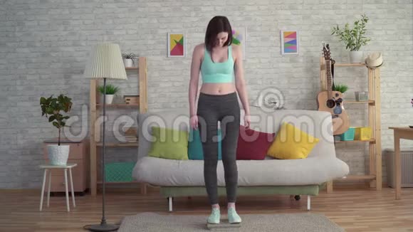 穿着运动服的痛苦的年轻女子在地板秤上测量她的体重视频的预览图