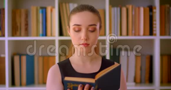 年轻成功的红头发女学生在室内图书馆阅读一本带有书架的书视频的预览图
