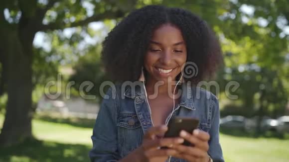 一位非洲裔美国年轻女性的笑脸她的耳朵里戴着耳机享受着聊天和移动的乐趣视频的预览图