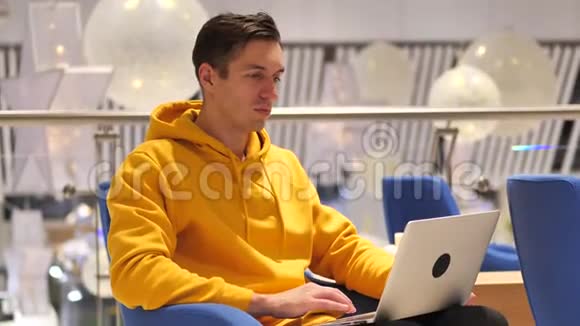 年轻人坐在咖啡厅时在笔记本电脑上想着震惊穿着黄色连帽衫的男人被他在电脑上看到的东西震惊了视频的预览图