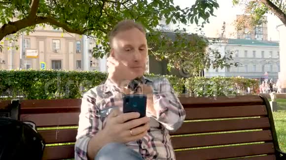 白种人坐在公园里坐在长凳上听耳机音乐视频的预览图