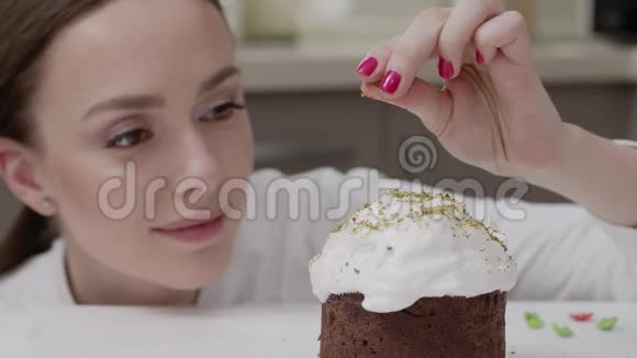 在专业厨房里穿着白色长袍的糖果女人装饰复活节蛋糕用开心果洒面包屑视频的预览图