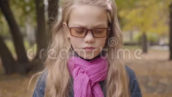 一个愤怒的白人少女站在秋天公园看镜头的肖像女学生视频的预览图
