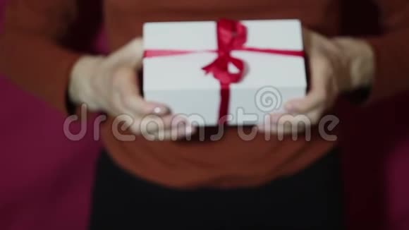 美丽的女孩在一个白色的盒子里拿出一份礼物上面有一条红色的丝带美丽的姑娘双手捧着新年礼物放在一个白盒子里视频的预览图