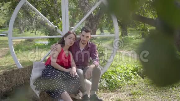 可爱的年轻女人和男人坐在花园里那家伙拥抱了他的女朋友情绪化的女人告诉她男朋友视频的预览图