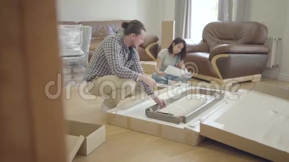 年轻的白人家庭在客厅里拆包幸福的一对夫妇装修他们的新房子开始视频的预览图