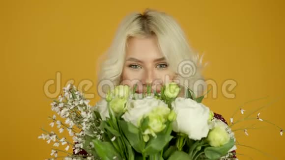 欢乐的金发女郎微笑着嗅着鲜花的正面景色视频的预览图