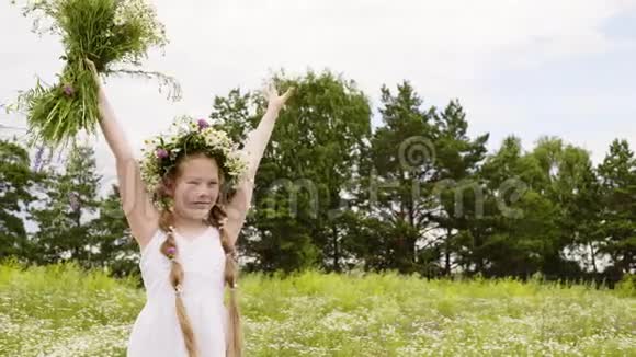 花圈里的少女举起双手手里拿着绿野上的草甸花快乐的女孩双手抱着头视频的预览图