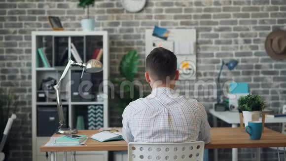 年轻人伸展双臂放松坐在办公桌前的后景视频的预览图