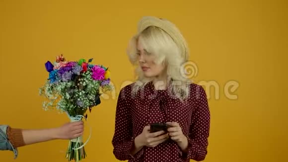 戴帽子的金发女孩使用智能手机拒绝黄色背景的花束视频的预览图