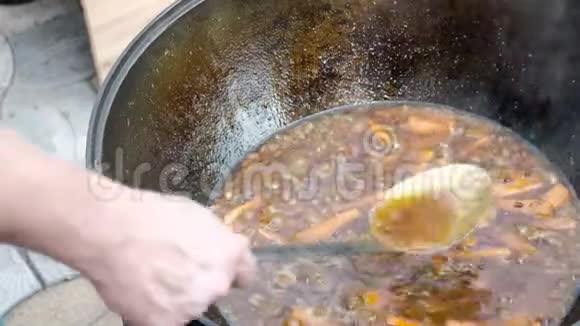 在大锅里煮热食厨师手搅动一个金属勺子里面有肉和胡萝卜特写镜头民族美食视频的预览图
