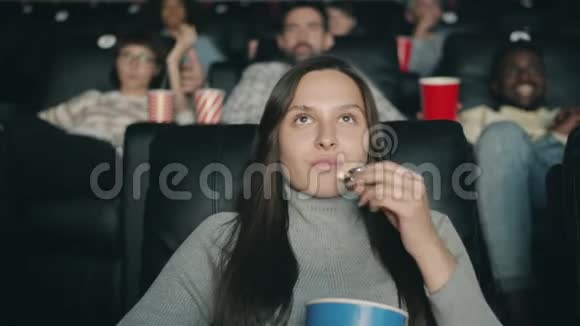 在电影院里漂亮的黑发女人在享受电影的缓慢动作笑着吃爆米花视频的预览图