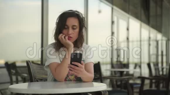 戴着耳机看智能手机的年轻女性视频的预览图