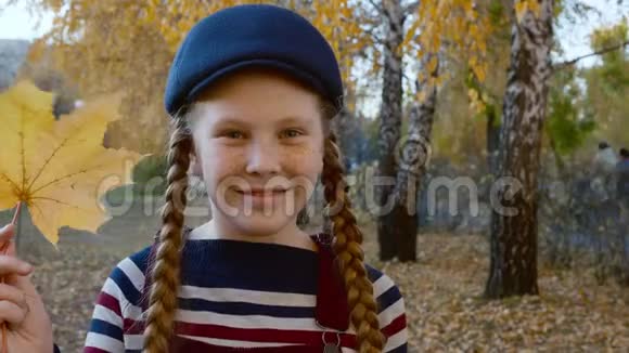 肖像少年女孩手里拿着黄色枫叶近脸微笑着面对秋天公园里快乐的女孩红色视频的预览图