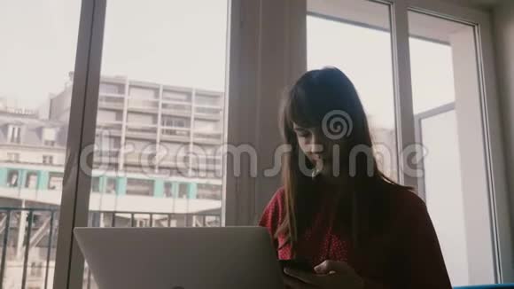 快乐自信的白种人年轻女商人在巴黎的大窗户上使用笔记本电脑和智能手机火车经过视频的预览图