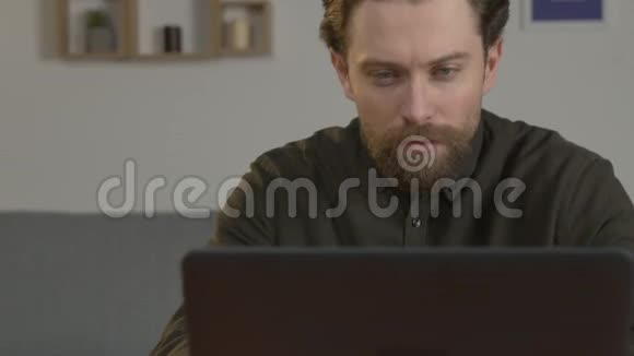 一个留着胡子的白人坐在一张桌子旁在笔记本电脑上工作在家里处理文件关门视频的预览图