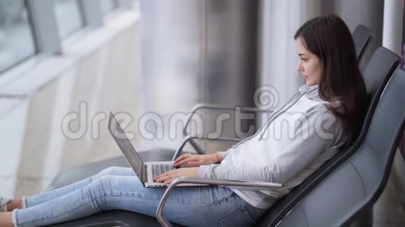 年轻女子坐在候机室用笔记本电脑在机场工作视频的预览图