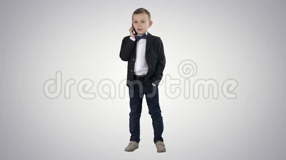 可爱的小男孩在他的智能手机上说话站在一套黑暗的西装梯度背景视频的预览图