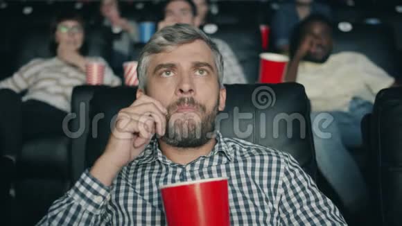 头发花白的男人在电影院里嚼爆米花看恐怖电影视频的预览图