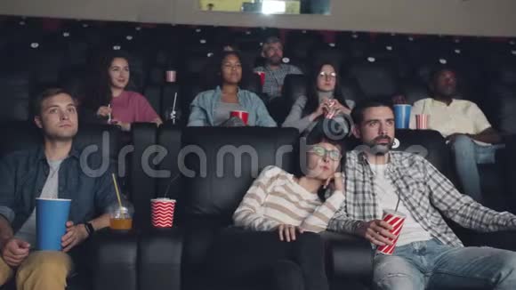 有魅力的男人和女人坐在电影院里吃零食和饮料看电影视频的预览图