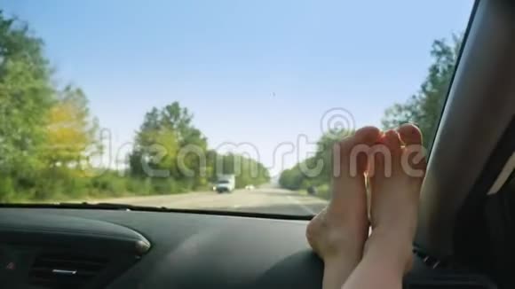 女性双脚放在汽车的仪表板上从乘客座位的侧面暑假和旅游的概念视频的预览图