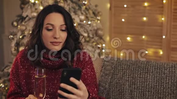 美丽的年轻女子端着香槟酒杯在圣诞树旁喝着酒背景下闪耀着灯光视频的预览图