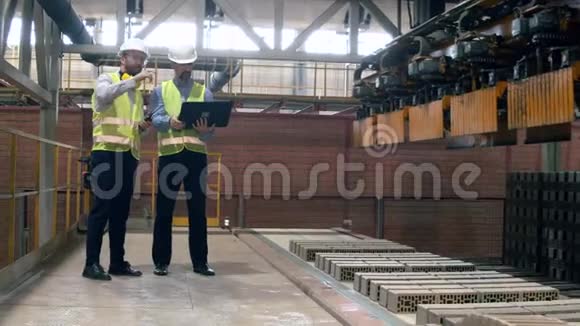新鲜的砖块沿着皮带移动两名工业工程师工人们正在观察它视频的预览图