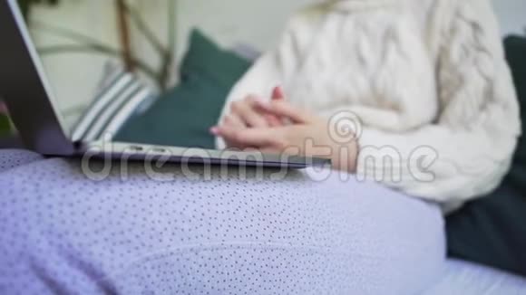 一个女人在家里结冰穿着白色针织毛衣在笔记本电脑上工作模糊概念特写视频的预览图