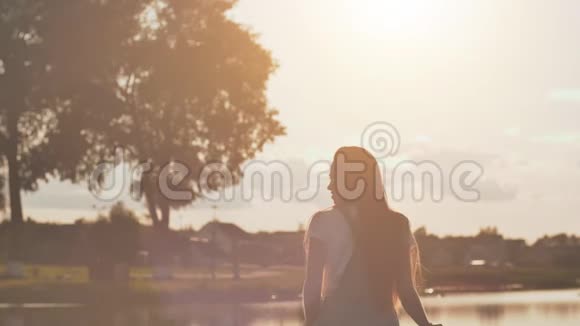 长头发的女孩心情很好在一个温暖的夏天晚上在湖边视频的预览图