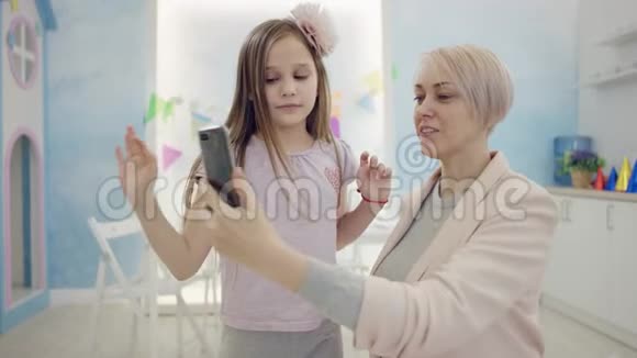 快乐的成年女性和她的小女儿在智能手机摄像头上自拍同时在镜头前拥抱她视频的预览图