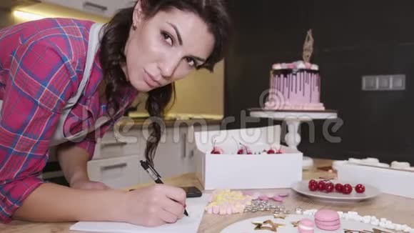 这位女糖果师正在写一份自制的美味生日蛋糕的食谱视频的预览图