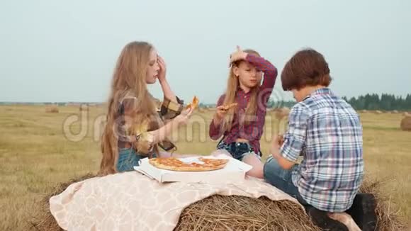 在收割场的干草堆上吃披萨的青少年朋友年轻女孩和男孩在乡村野餐时吃披萨视频的预览图