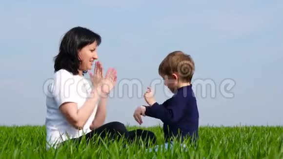 幸福的家庭妈妈和孩子坐在绿草上玩耍互相拍打着巴蒂视频的预览图