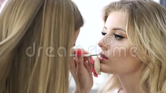 化妆师在沙龙里画年轻女人嘴唇视频的预览图