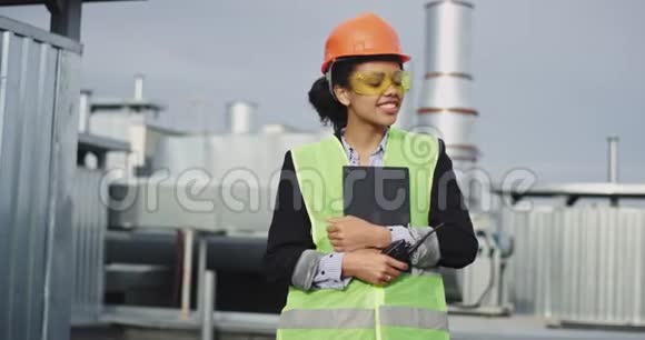 在工地上美丽的微笑着戴着安全装备头盔和眼镜的非洲女工程师视频的预览图