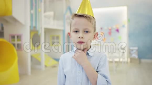 一个戴着假锥帽在游戏室镜头前摆姿势的悲伤小男孩视频的预览图