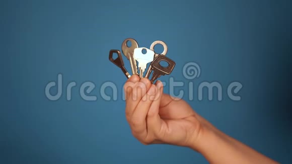 用不同的钥匙特写手女人手拿着蓝色背景上的五把钥匙视频的预览图