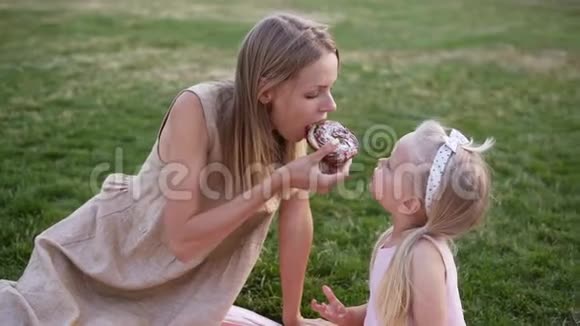 母亲和一个小女儿的肖像一起在城市公园野餐他们咬一口美味的甜甜圈视频的预览图