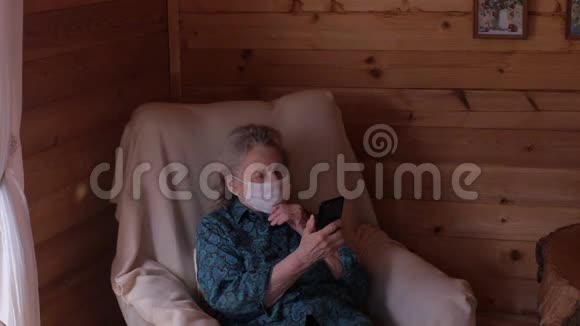 一位戴着医用面具的老年妇女试图整理智能手机的中间视角冠状病毒大流行视频的预览图
