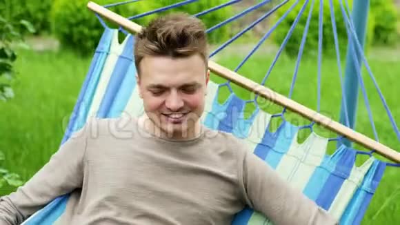 一个快乐男人的特写肖像躺在花园的吊床上微笑着放松视频的预览图