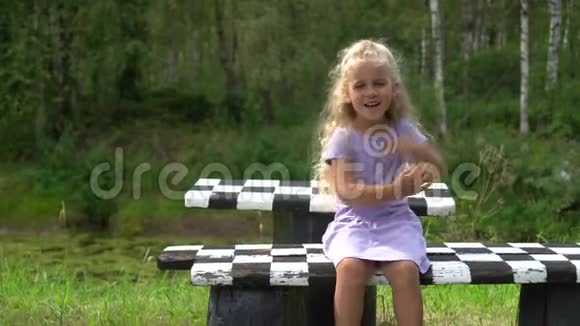 有趣的小女孩坐在格子长凳上在公园里笑视频的预览图