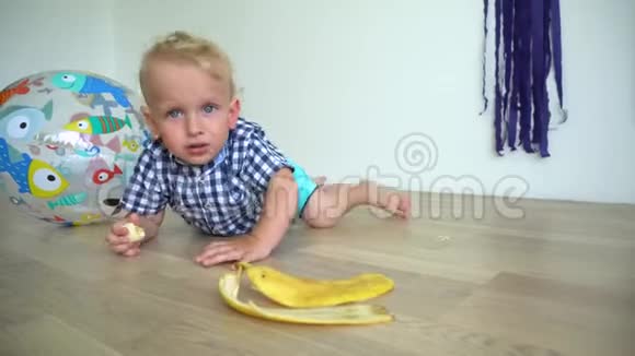 两岁的孩子坐在地板上吃黄色的香蕉万向节运动视频的预览图