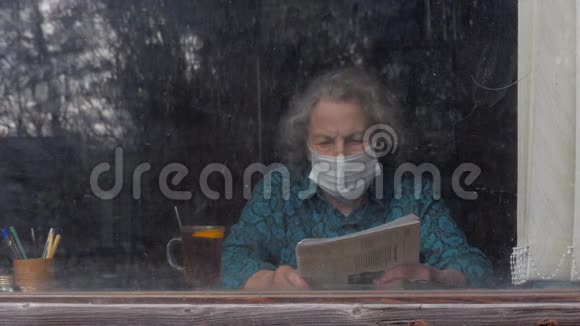 年迈的老年妇女戴着面具坐在家里看报纸检疫呆在家里冠状病毒仍然是视频的预览图