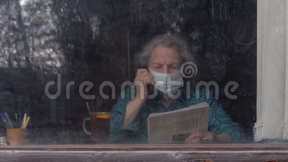 戴着医用口罩的老年妇女坐在家里打电话大流行冠状病毒科维德19呆在家里视频的预览图