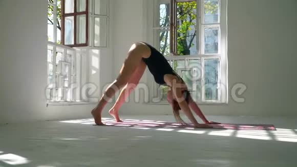 身材苗条的白人妇女站在大房间的垫子上练习瑜伽站在下面的那个女孩视频的预览图
