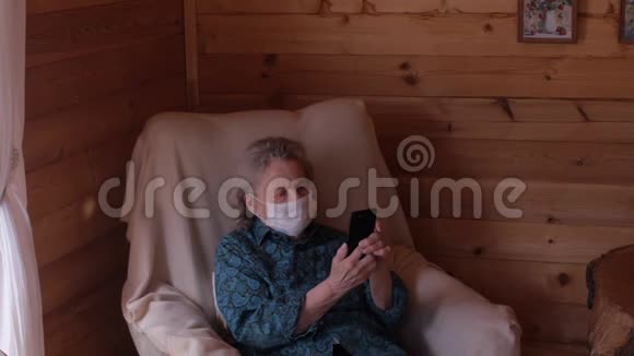 一位坐在椅子上的老年妇女调整医疗面罩并试图了解智能手机冠状病毒大流行留h视频的预览图