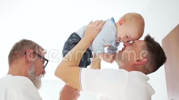 同一个家庭的快乐男人三个人祖父父亲和孙子父亲天男人用白色拥抱婴儿视频的预览图