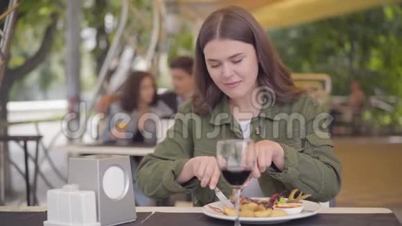 可爱的年轻女子穿着休闲服装在街头咖啡馆吃肉喝红酒享受美食放松的女孩视频的预览图