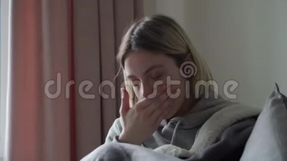金发女孩坐在灰色的沙发上患有病毒性疾病手掌咳嗽Orvi的症状视频的预览图