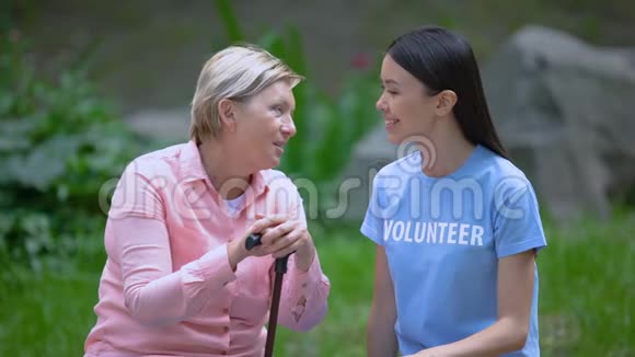 老年女性患者手杖说话年轻志愿者坐在户外视频的预览图